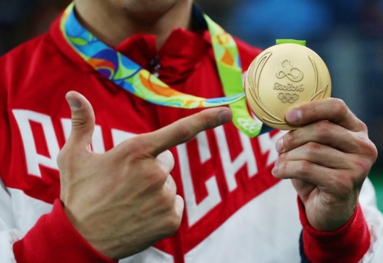 Держит в руках медаль спортсмен